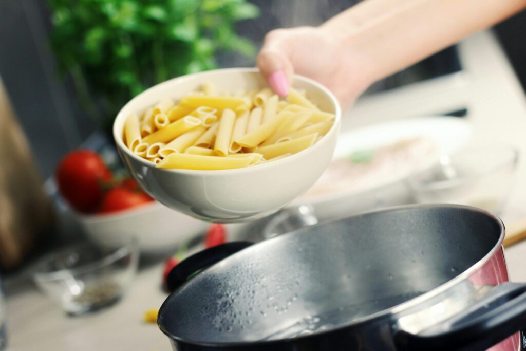 A fresh bowl of penne pasta ready to be boiled in a stainless steel pot.
